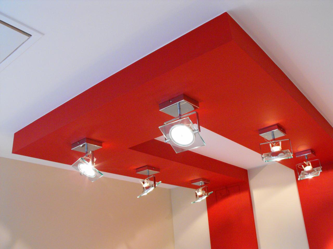 Pomieszczenie z czerwonym sufitem podwieszanym, oświetlonym przez sześć kwadratowych, szklanych reflektorów, z białymi i beżowymi ścianami.