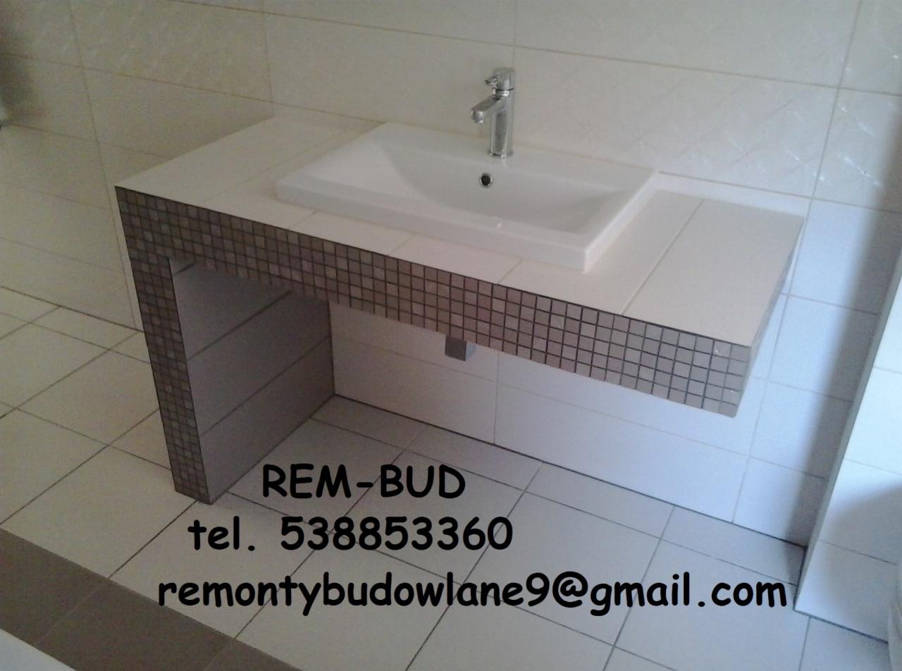 Nowoczesna umywalka nablatowa z chromowaną baterią, osadzona na blacie wykończonym mozaiką w odcieniach szarości, zamontowana w wykafelkowanej łazience.