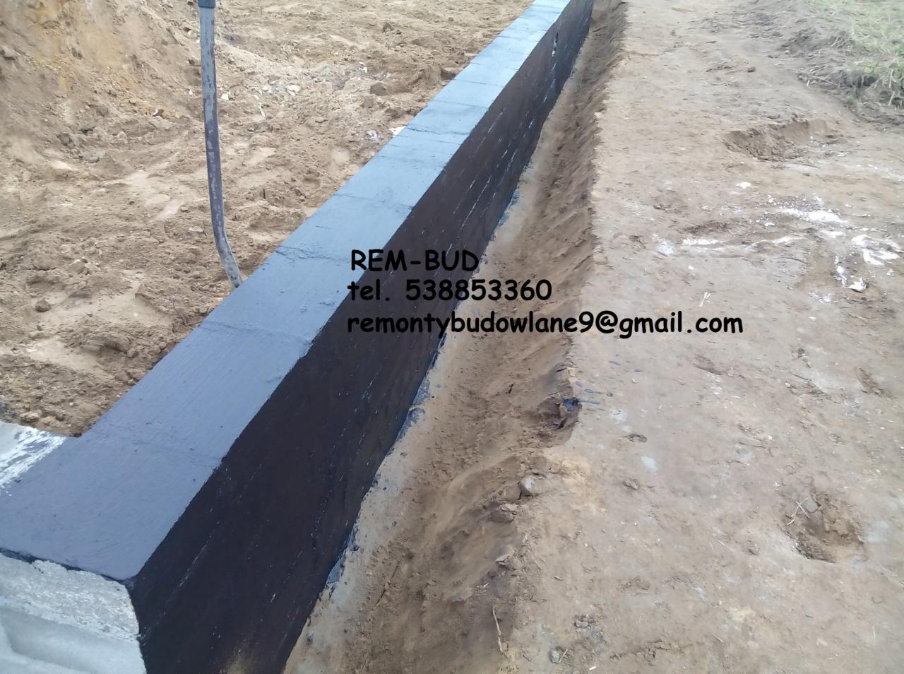 Murowanie fundamentów: świeżo zaizolowany, czarny fundament z betonu komórkowego, widoczny rów wykopany w ziemi, izolacja przeciwwilgociowa, kontakt do firmy REM-BUD na zdjęciu.