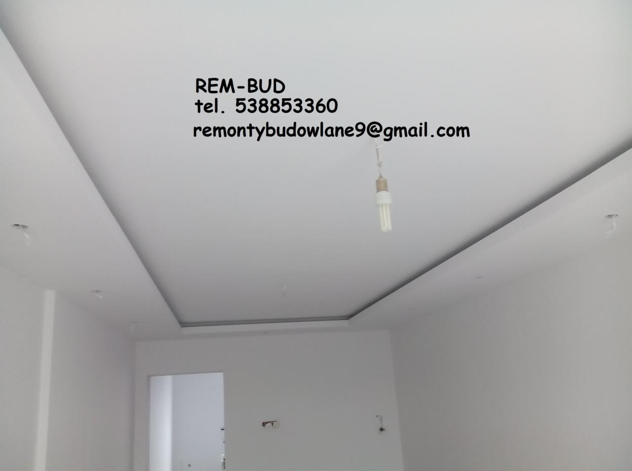 Wykończony sufit podwieszany z wnęką oświetleniową, z widocznym adresem e-mail i numerem telefonu firmy REM-BUD na górze kadru, w tle surowa żarówka wisząca na kablu.