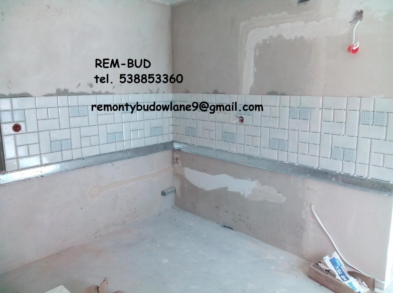 Ściana łazienki w trakcie kładzenia płytek, widoczne logo firmy REM-BUD, numer telefonu i adres email na ścianie, surowy stan pomieszczenia, nieukończone fugi, wystające kable.