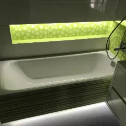 Biała wanna z zielonymi paskami i podświetleniem LED, umieszczona w łazience z zielonymi płytkami w kropki i chromowaną armaturą.