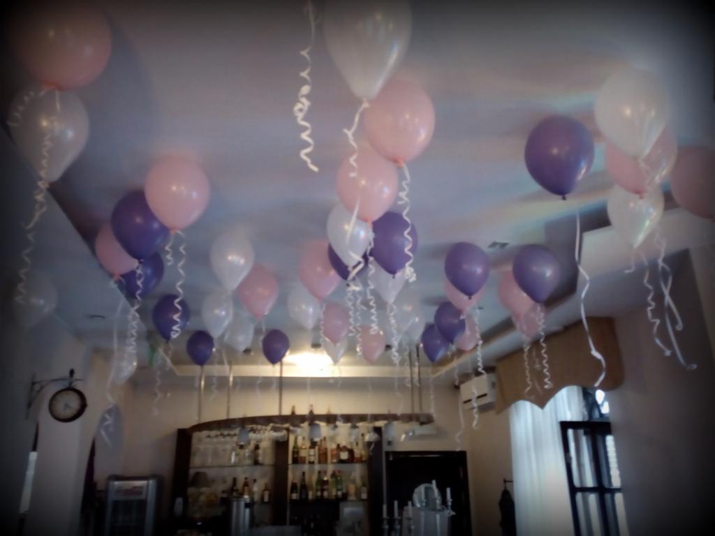Dekoracja sali balonami w odcieniach różu, fioletu i bieli, z kręconymi wstążkami, widok na bar z alkoholem w tle.
