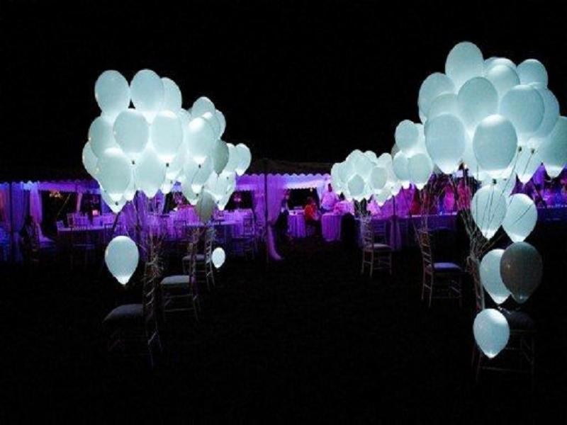 Uroczyste oświetlenie plenerowe: Balony z wewnętrznym światłem, ustawione wzdłuż ścieżki, prowadzą do namiotu z fioletowym oświetleniem, gdzie przygotowano stoły i krzesła.