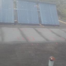 macedonska - Montaż paneli słonecznych na płaskim dachu pokrytym papą, widoczne czerwone oznaczenia na papie, w tle budynki i drzewa w lekkiej mgle.