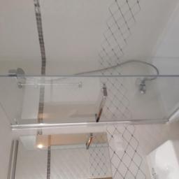 macedonska - Szklana kabina prysznicowa z przesuwanymi drzwiami zamontowana w łazience z białymi płytkami i dekoracyjnym pasem mozaiki, widoczny również zestaw prysznicowy