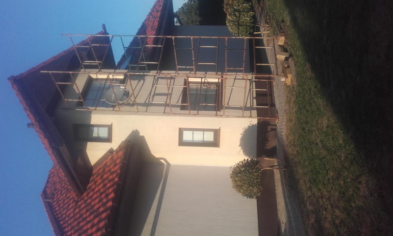 Dom jednorodzinny z nałożonym rusztowaniem podczas prac remontowych, widoczne świeżo pomalowane elewacje w odcieniach beżu i szarości.