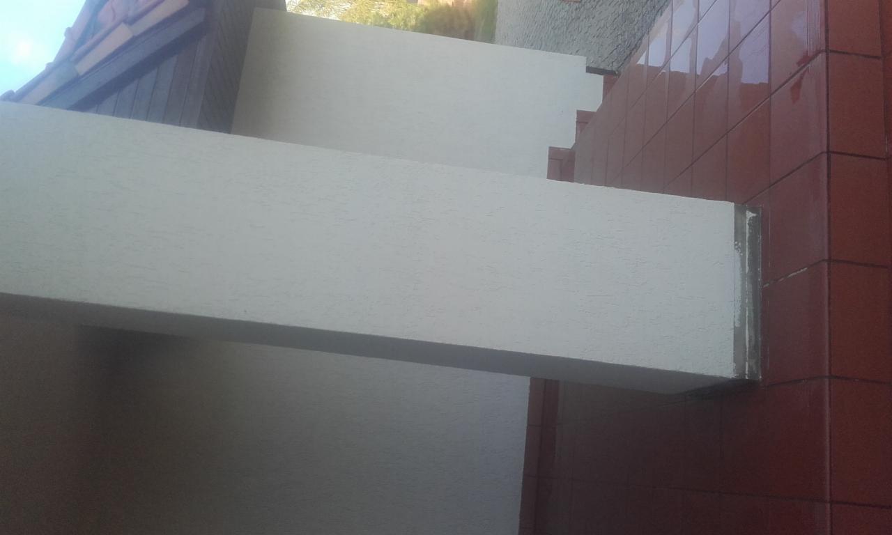 Balkon z beżową, chropowatą balustradą i brązową okładziną ścienną z płytek ceramicznych, widziany z dołu.