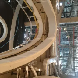 Wnętrze w trakcie wykańczania z widocznymi łukowymi elementami konstrukcyjnymi pokrytymi gładzią, rusztowaniami i instalacjami.