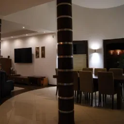 Przestronny salon z jadalnią, widoczne kolumny dekoracyjne, telewizor na ścianie, stół z krzesłami i parkiet przechodzący w płytki.