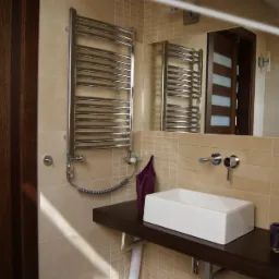 Nowoczesna łazienka z beżowymi płytkami, prostokątną umywalką nablatową, grzejnikiem drabinkowym i drewnianymi drzwiami z mlecznymi szybami w tle.