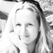 Portret kobiety z blond włosami, opierającej podbródek na dłoni. Zdjęcie czarno-białe, z naturalnym oświetleniem i delikatnym uśmiechem.