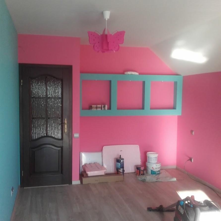 Pokój po malowaniu: różowe ściany, turkusowe akcenty, drewniane panele, drzwi z ciemnego drewna, lampa-motyl, puszki z farbą i akcesoria na podłodze.