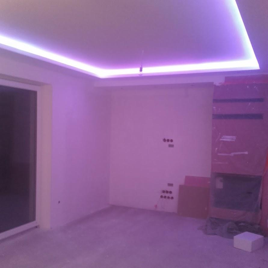 Pokój w trakcie przygotowania, z podświetlanym sufitem i widocznymi puszkami elektrycznymi na ścianie, zabezpieczony kominek w rogu.