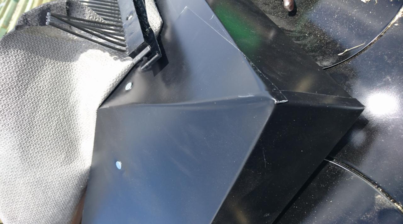 Element rynny w kolorze czarnym, widoczne łączenie blach, fragment dachu w tle oraz szara tkanina.