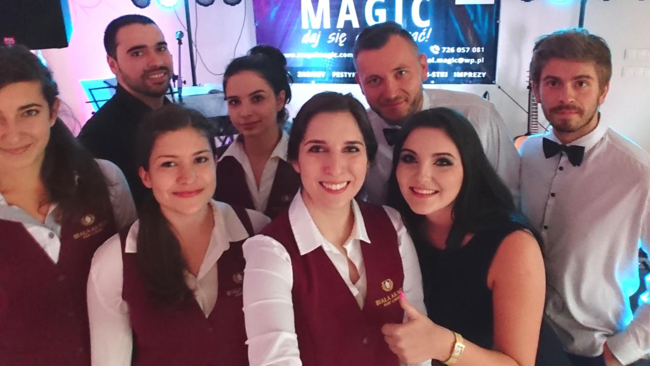 Zespół muzyczny 'Biała Akademia' w strojach scenicznych pozuje do zdjęcia grupowego na tle sceny z napisem 'MAGIC' i oświetleniem dyskotekowym.