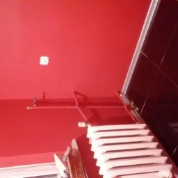 Czerwona łazienka z czarnymi błyszczącymi płytkami, widoczny biały grzejnik i fragment instalacji hydraulicznej w kolorze ściany.