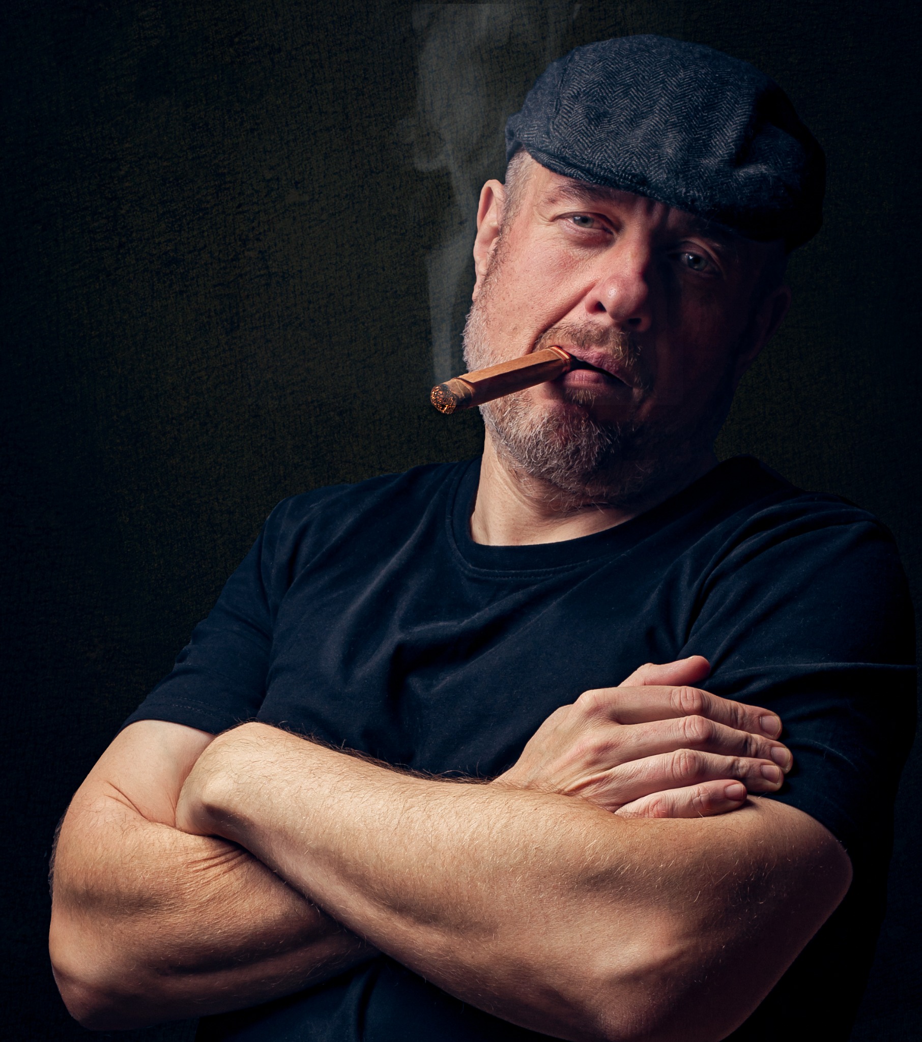 Portret mężczyzny w kaszkiecie, z zamyślonym wyrazem twarzy, palącego cygaro na ciemnym tle.
