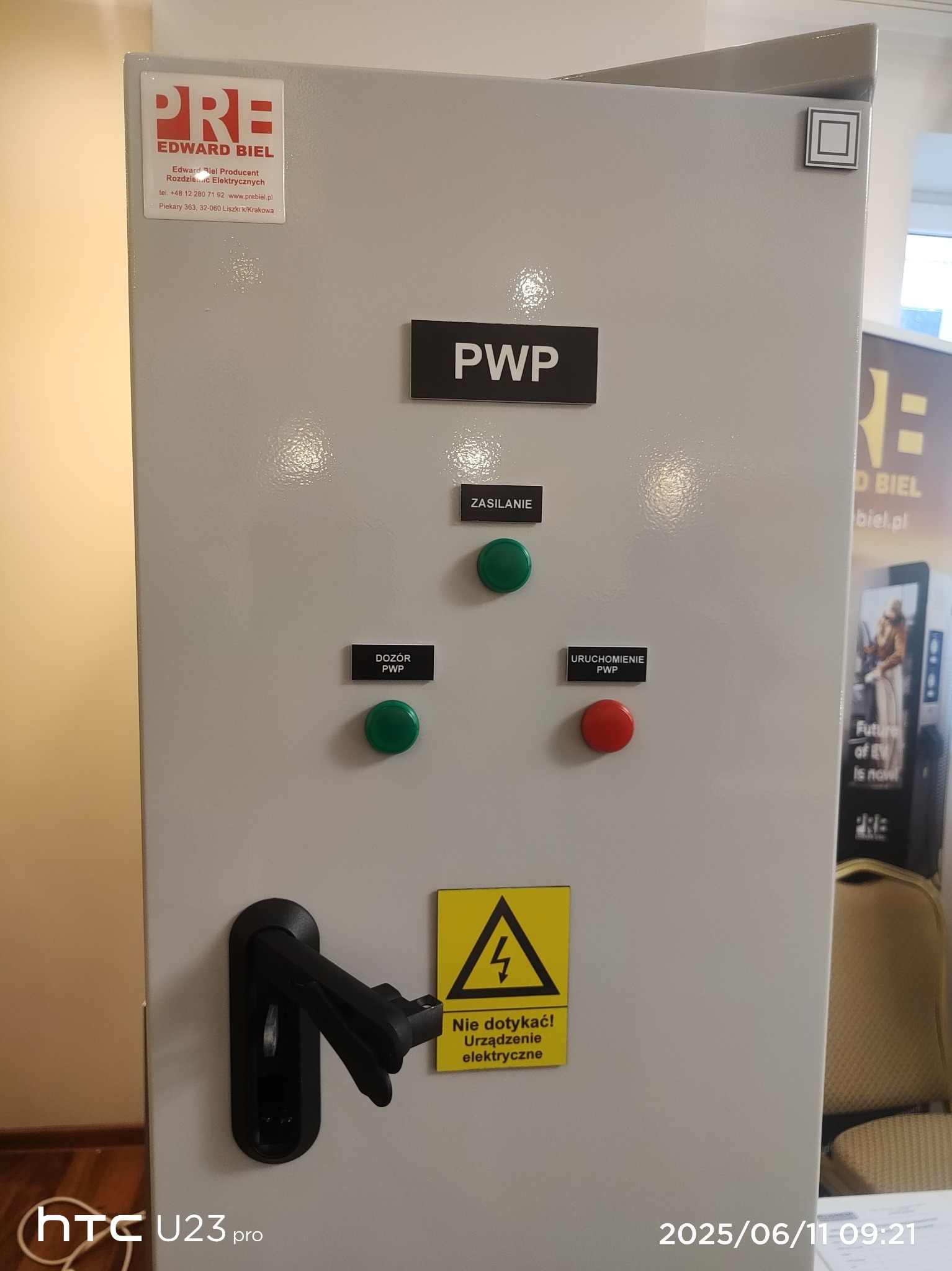 Szara szafa sterownicza PWP (przeciwpożarowy wyłącznik prądu) z zielonymi i czerwonymi przyciskami, tabliczkami z opisami i ostrzeżeniem o napięciu.