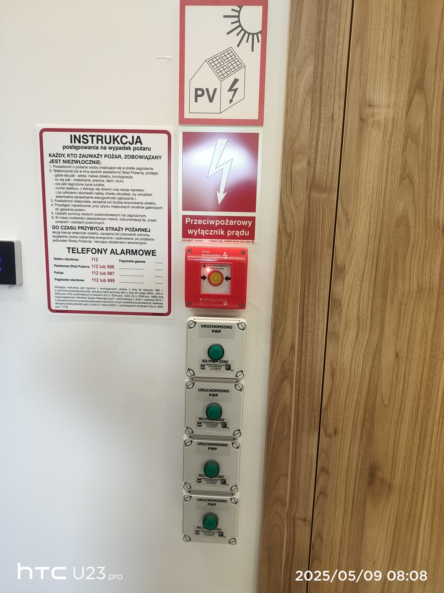 Tablica z instrukcją ppoż., wyłącznik prądu i przyciski PWP. Znaki informacyjne, instrukcje i urządzenia związane z bezpieczeństwem pożarowym w budynku.