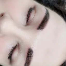 Zbliżenie na twarz kobiety z zamkniętymi oczami, prezentujące brwi po zabiegu stylizacji i henny, z widocznymi pojedynczymi włoskami i delikatnym makijażem.