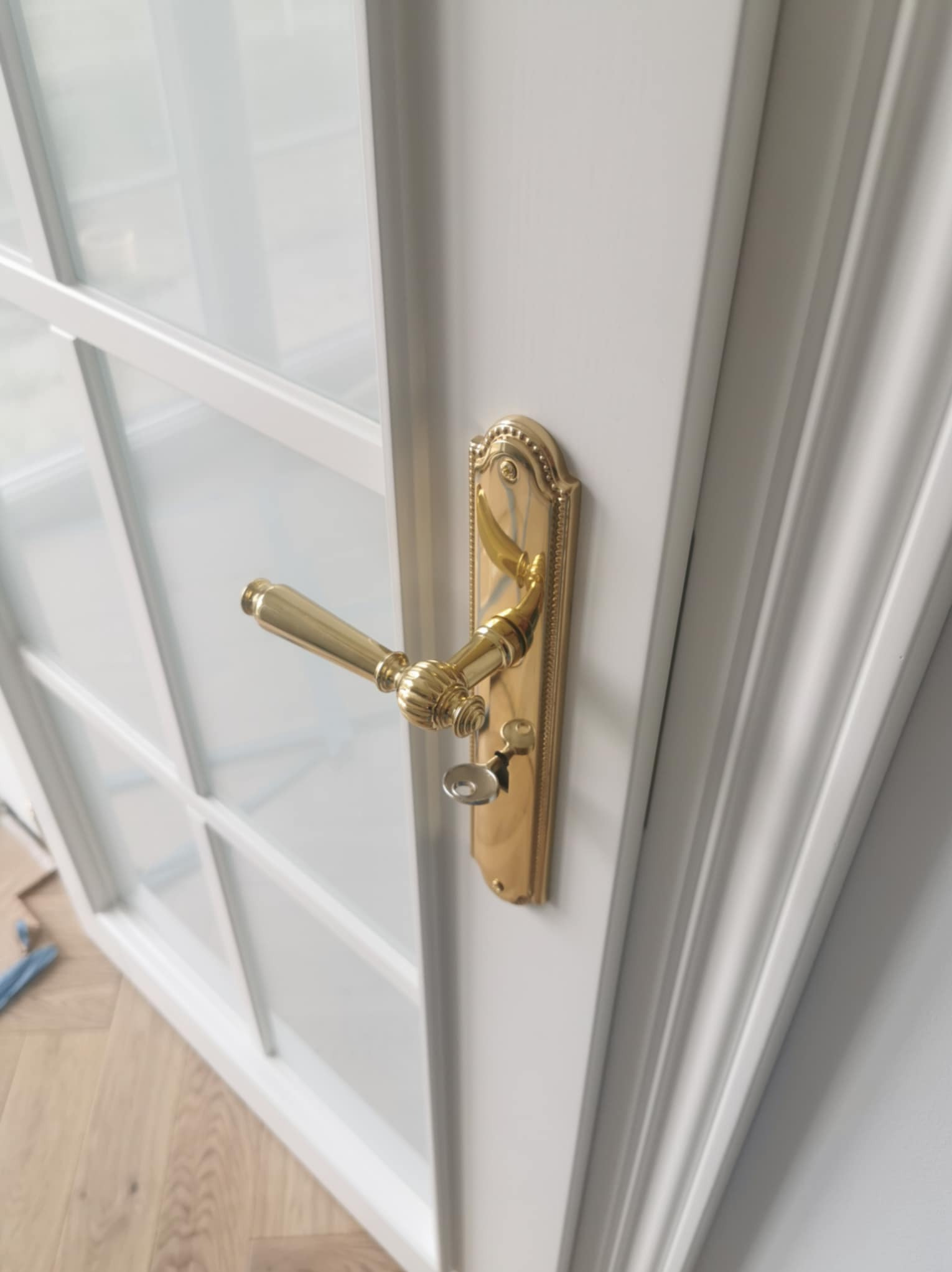 Białe skrzydło drzwiowe z szybami i złotą klamką, widok z bliska. Detal wykończenia w Skrzydlnej. Klasyczny design, eleganckie okucia.