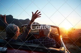 Para starszych osób podróżuje kabrioletem o zachodzie słońca, ręce uniesione w geście radości, widok na góry w tle.