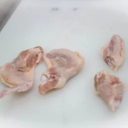 Surowe, pojedyncze skrzydełka kurczaka ułożone na białej, czystej desce do krojenia.