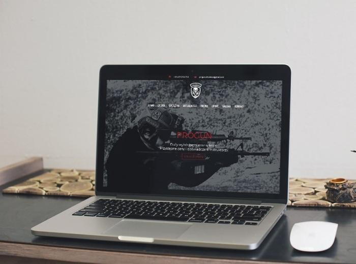 Laptop wyświetlający stronę internetową firmy Progun z motywem militarnym, na biurku obok myszka.