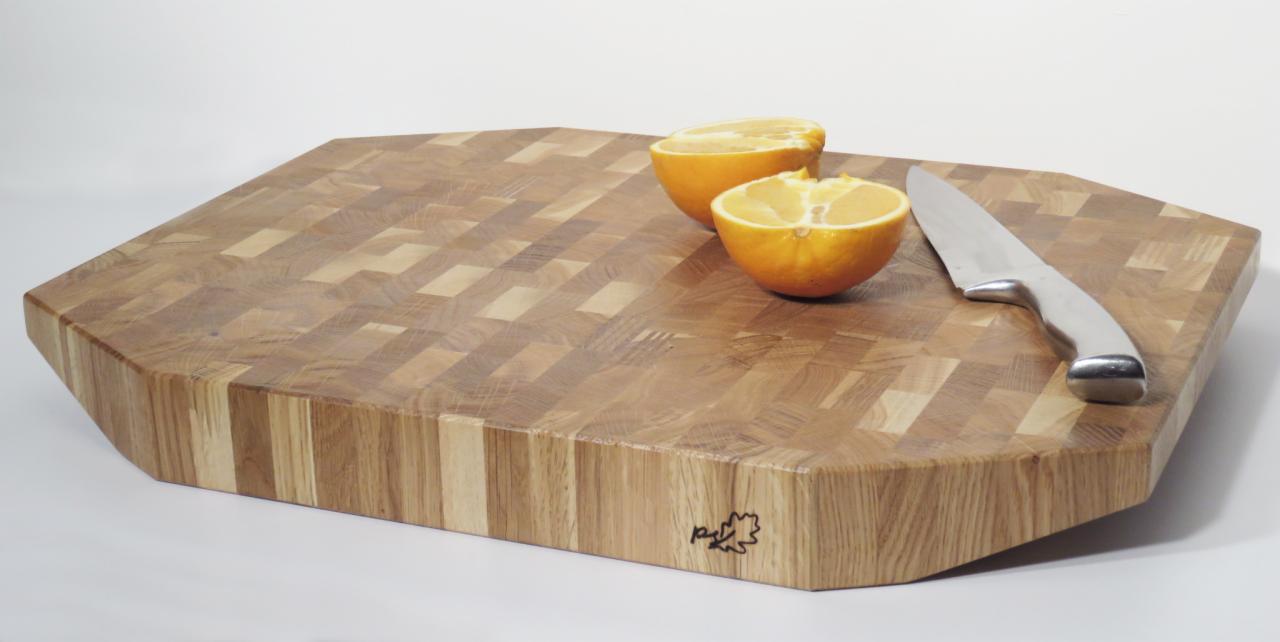 Wieloboczna deska do krojenia z drewna klejonego, z widocznym wzorem kostki i logo w rogu, na której leżą dwie połówki pomarańczy i nóż z metalową rękojeścią.