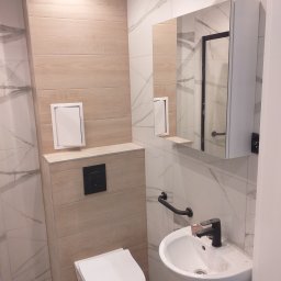 Elba - Nowoczesna łazienka z wiszącą toaletą, umywalką nablatową z czarną armaturą i lustrem z szafką, wykończona płytkami imitującymi drewno i marmur.