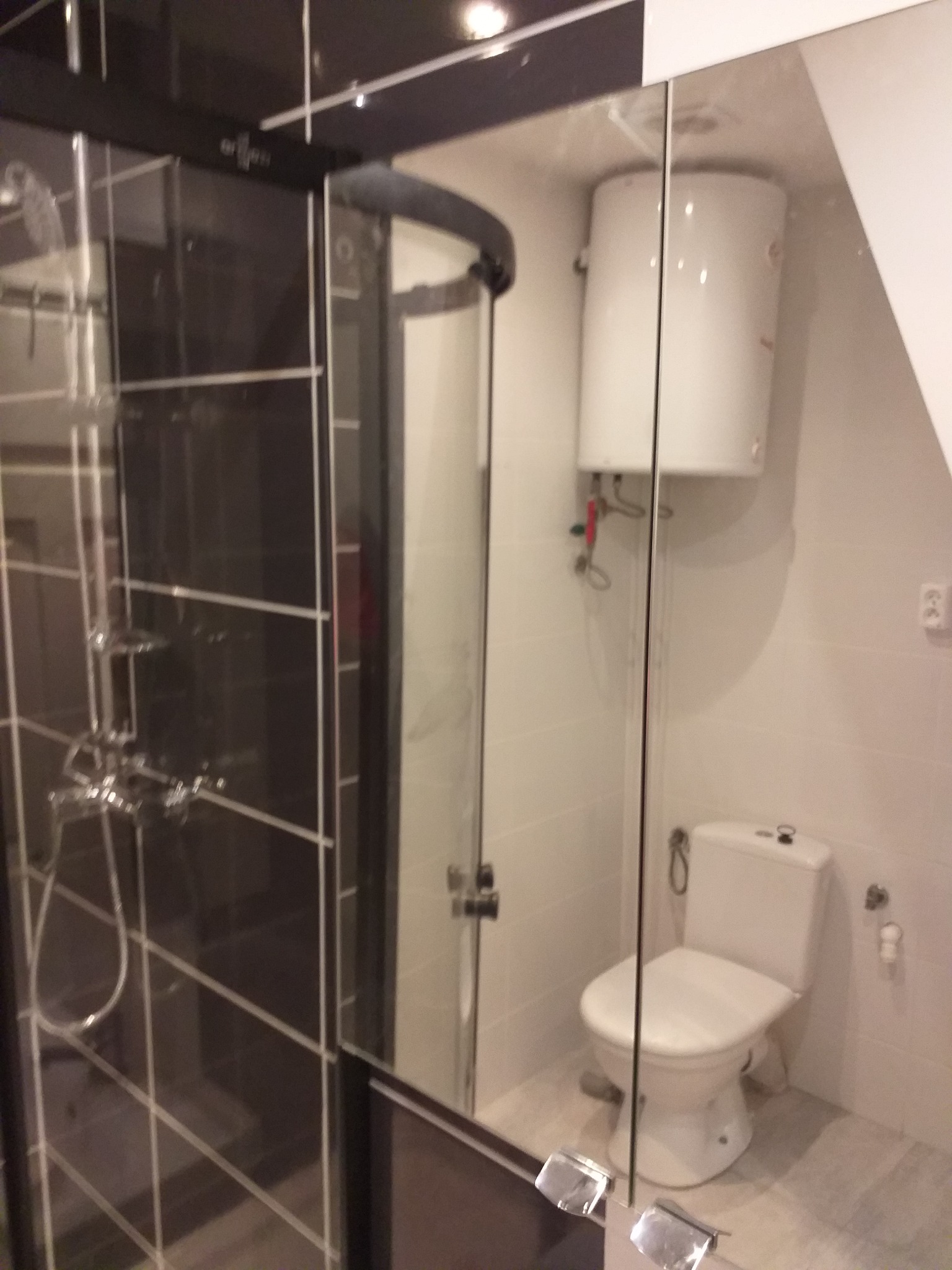 Nowoczesna łazienka z kabiną prysznicową typu walk-in z ciemnymi profilami, widoczny biały bojler i toaleta.