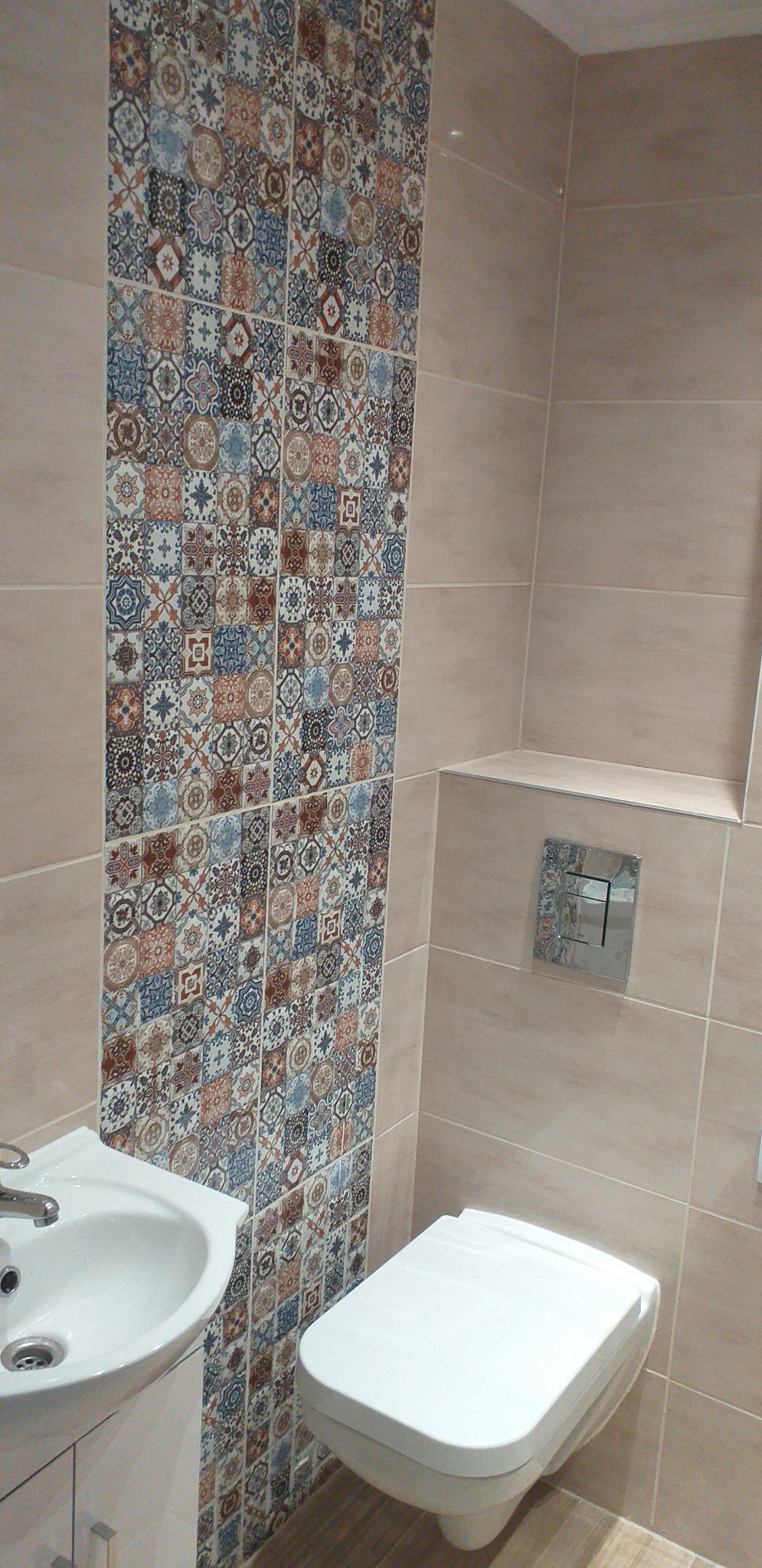 Wykończona łazienka z beżowymi płytkami i dekoracyjnym pasem płytek patchworkowych za umywalką i toaletą podwieszaną.