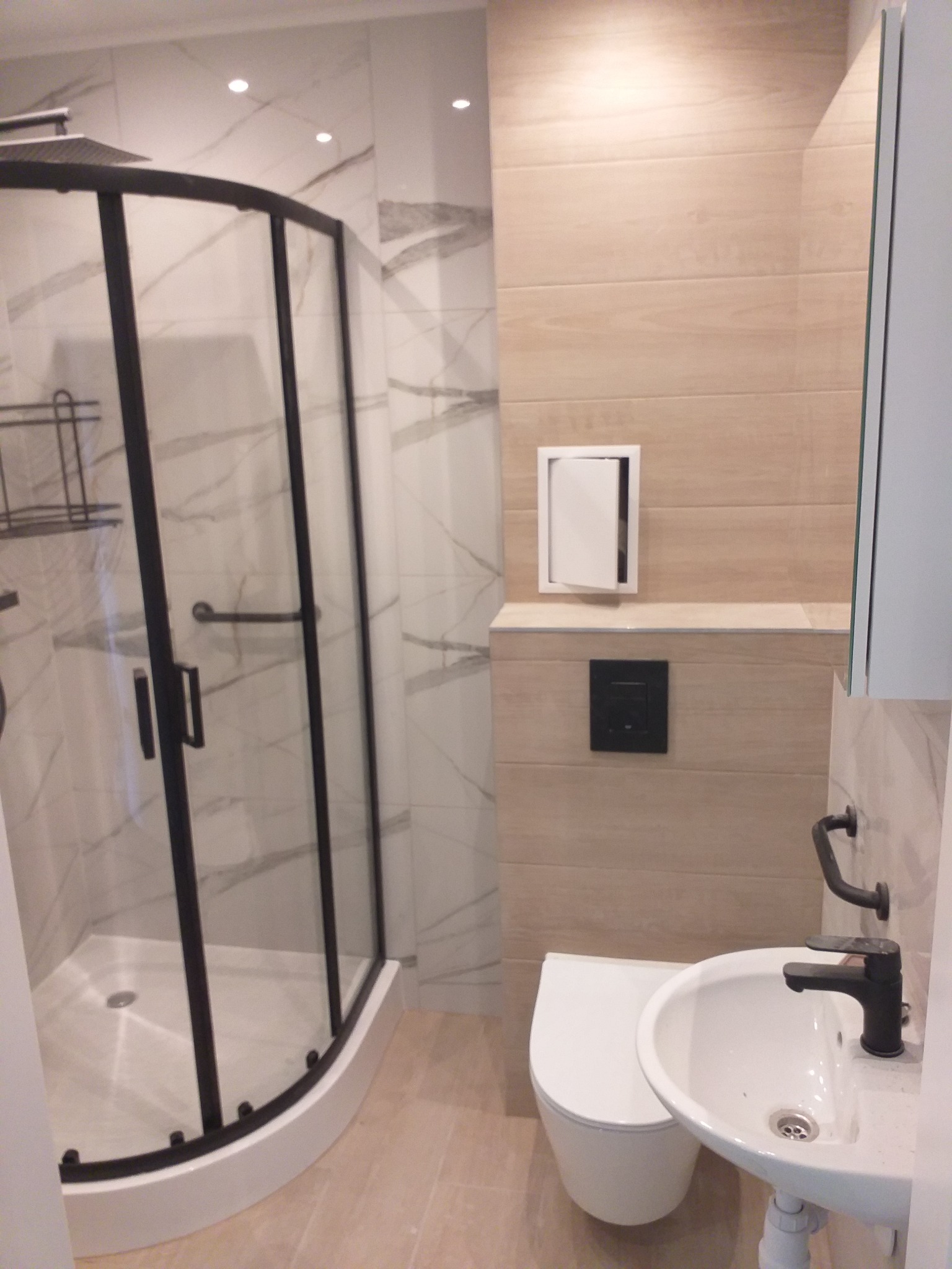 Nowoczesna łazienka po remoncie w Zamościu: kabina prysznicowa z czarną ramą, umywalka z czarną armaturą, toaleta w jasnych, beżowo-szarych tonacjach.