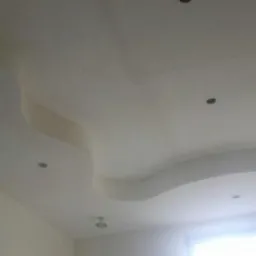 Biały sufit podwieszany z dekoracyjnymi, łukowatymi elementami i otworami na oświetlenie punktowe, widziany pod kątem z dołu.