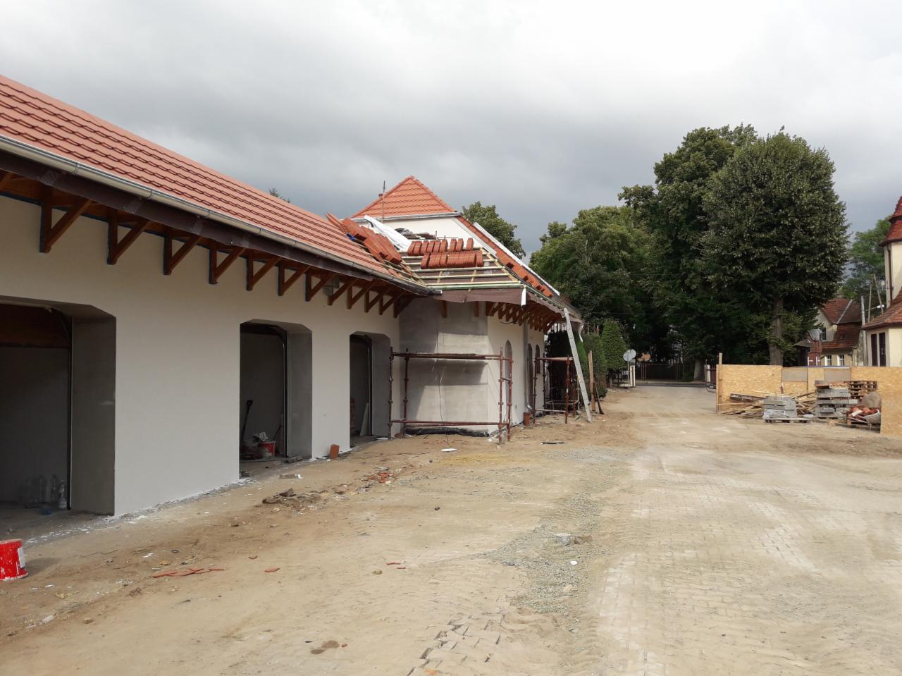 Budynek w trakcie renowacji elewacji i wymiany pokrycia dachowego, widoczne rusztowania, nowe dachówki częściowo ułożone, świeżo otynkowana ściana, teren budowy z materiałami budowlanymi.