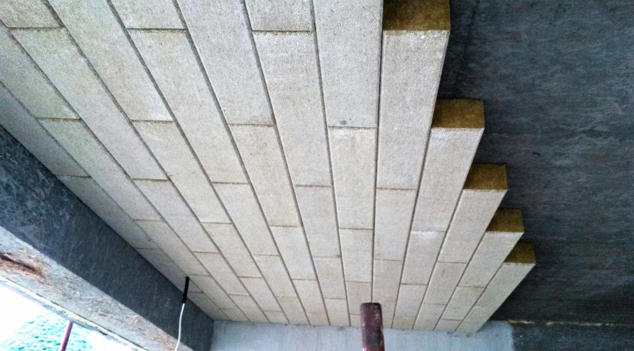 Płyty izolacyjne z wełny mineralnej układane na poddaszu, widok od dołu, surowy betonowy strop w tle.