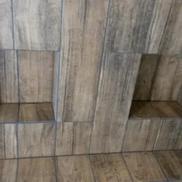 Dwa kwadratowe wnęki w ścianie wyłożonej brązowymi płytkami imitującymi drewno z szarymi fugami.