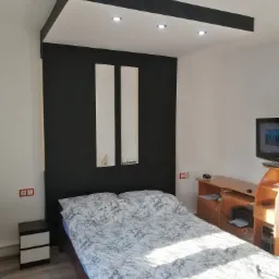 Sypialnia z łóżkiem, czarną ścianą z dwiema białymi wnękami z dekoracjami, podwieszanym sufitem z oświetleniem punktowym i drewnianymi meblami.