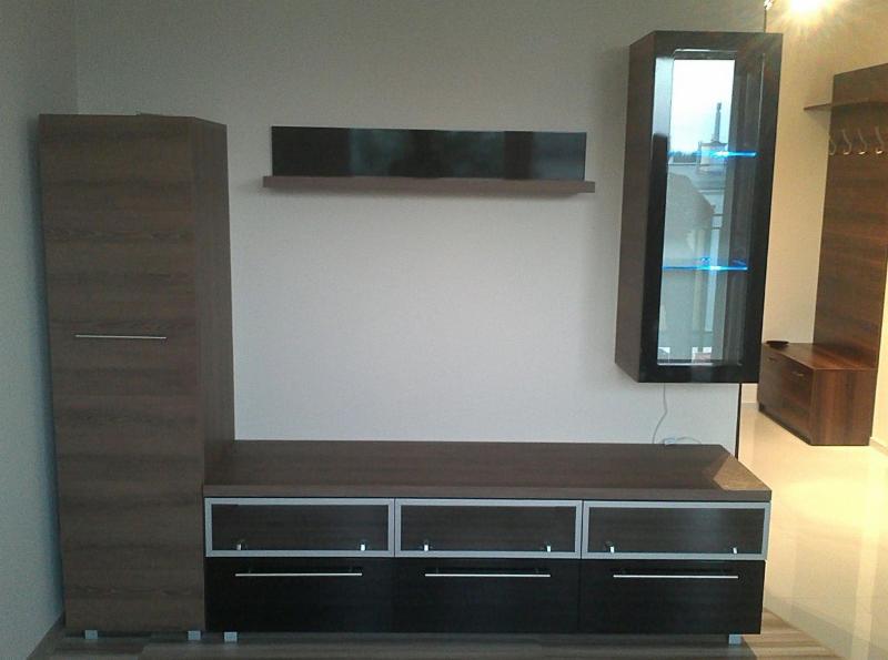 Zestaw mebli do salonu z szafkami wiszącymi i stojącymi w kolorach brązu i czerni, z oświetleniem LED w witrynie, na tle jasnej ściany.