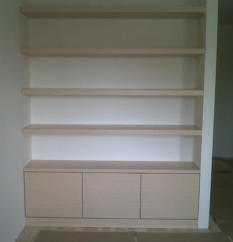 Jasna zabudowa meblowa z trzema szafkami i czterema półkami, wbudowana we wnękę, wykończona białą listwą po prawej stronie.
