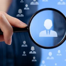 Dłoń trzymająca szkło powiększające nad ikonami sylwetek ludzi na niebieskim tle.