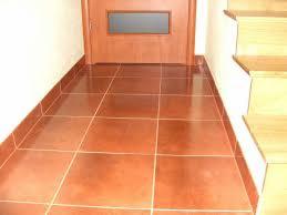 Błyszcząca, brązowa podłoga z płytek ceramicznych w korytarzu, widoczny fragment drewnianych schodów i drzwi z przeszkleniem.