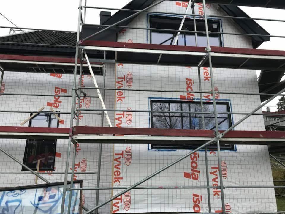 Dom w trakcie ocieplania, widoczne rusztowania, okna z czarnymi ramami, folia izolacyjna z nadrukiem Tyvek i Isola na elewacji