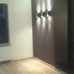 Jasne panele podłogowe w pustym pokoju z ciemnobrązową ścianą akcentującą oświetloną trzema lampami punktowymi, widok na okno i kaloryfer.