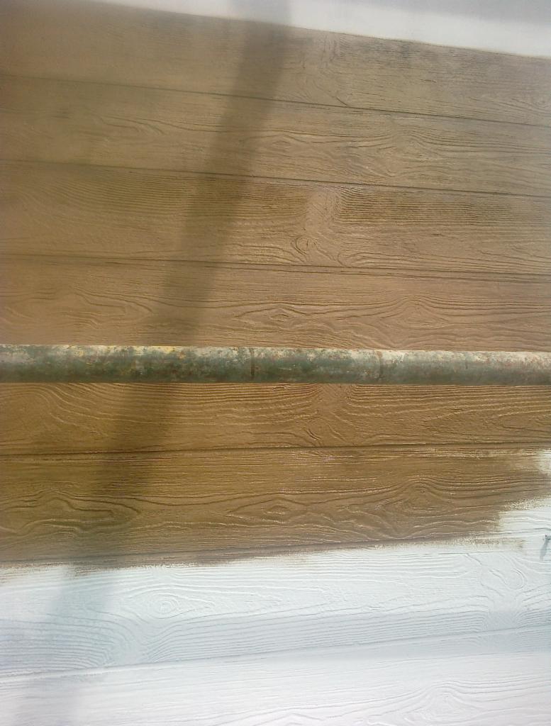 Brunatna elewacja z imitacją drewna, częściowo pomalowana na biało, z widoczną rurą rusztowania.