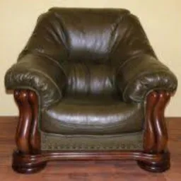 Zielony, skórzany fotel klubowy z ciemnobrązowymi, toczonymi nogami, stojący na drewnianej podłodze. Widoczne marszczenia i załamania skóry na siedzisku i oparciu.