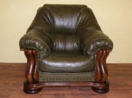 Zielony, skórzany fotel klubowy z ciemnobrązowymi, toczonymi nogami, stojący na drewnianej podłodze. Widoczne marszczenia i załamania skóry na siedzisku i oparciu.