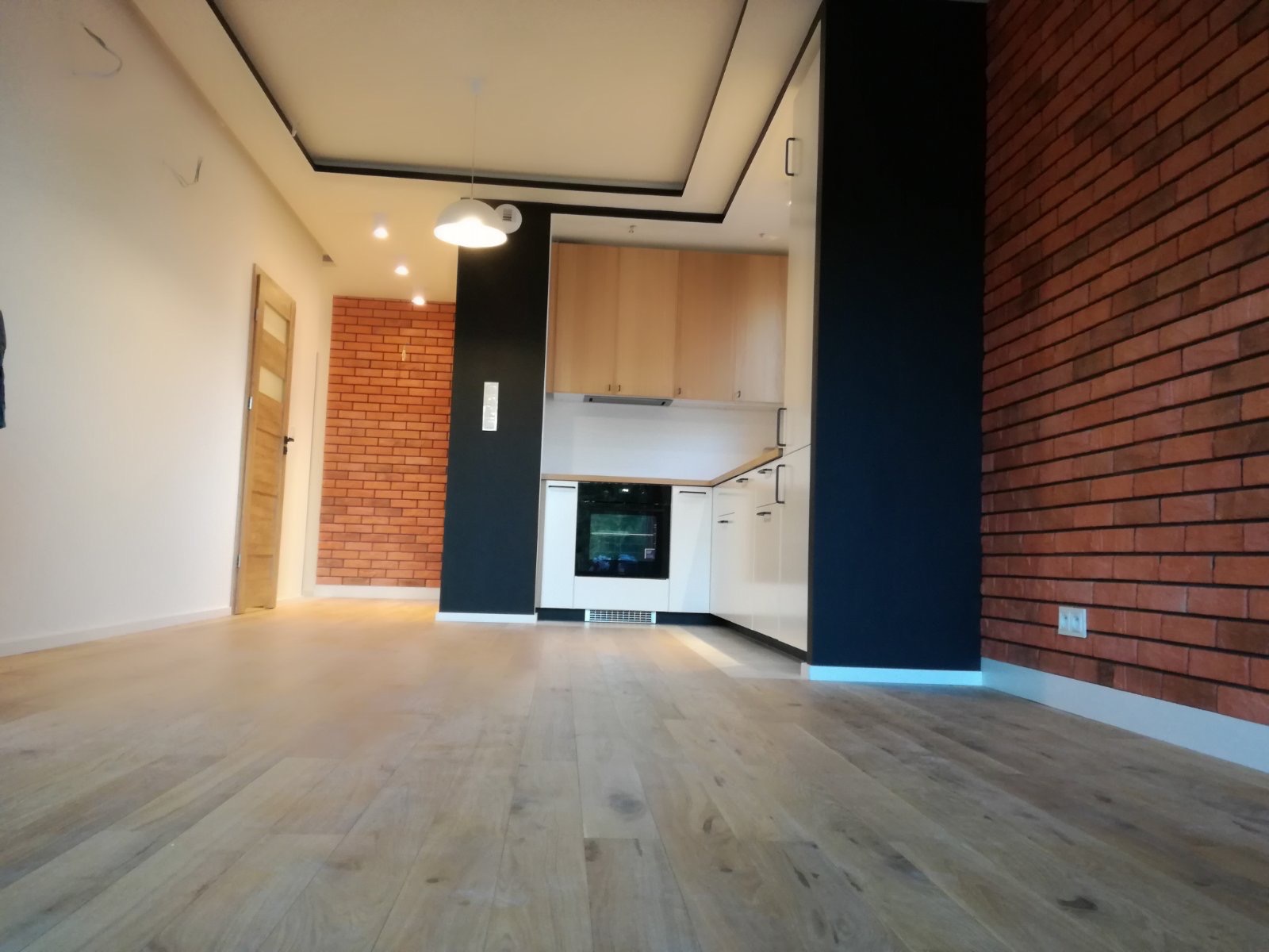 Nowoczesna kuchnia z drewnianymi podłogami, ceglaną ścianą i białymi szafkami, widok z niskiego kąta.