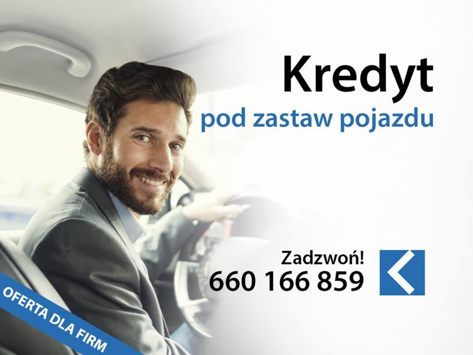 Uśmiechnięty mężczyzna w garniturze siedzi za kierownicą samochodu, obok niego napis 'Kredyt pod zastaw pojazdu' i numer telefonu.